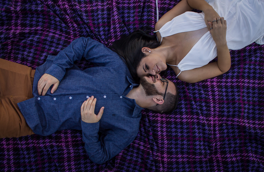 ENSAIO FOTOGRAFICO DE CASAL PRE WEDDING DEITADOS NA TOALHA  DE PIQUENIQUE ROXA AO AR LIVRE BEIJO MARINGA PARANA