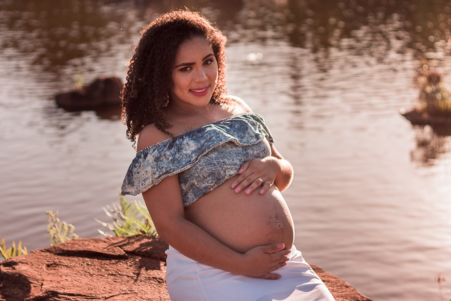 ENSAIO FOTOGRAFICO DE GESTANTES NO PARQUE DO JAPAO EM UMA TARDE ENSOLARADA EM MARINGA PARANA BRASIL NA IMAGEM A GESTANTE ESTA SENTADA EM UMA PEDRA COM UMA LAGOA DE FUNDO DESFOCADA