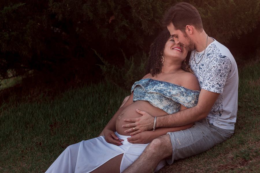 ENSAIO FOTOGRAFICO DE GESTANTES NO PARQUE DO JAPAO EM UMA TARDE ENSOLARADA EM MARINGA PARANA BRASIL NA IMAGEM O CASAL ESTA SENTADO NA GRAMA ENQUANTO O PAPAI FAZ CARINHO NA BARRIGA DA MAMAE QUE ESTA OLHANDO PARA ELE ENQUANTO SORRI