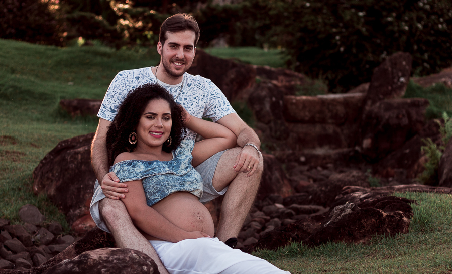 ENSAIO FOTOGRAFICO DE GESTANTES NO PARQUE DO JAPAO EM UMA TARDE ENSOLARADA EM MARINGA PARANA BRASIL NA IMAGEM O CASAL ESTA SENTADO EM UMA PEDRA OLHANDO DIRETAMENTE PARA A FOTO ENQUANTO SORRIEM