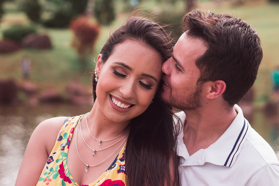 ENSAIO FOTOGRÁFICO PRÉ-WEDDING PRE WEDDING PREWEDDING DE CASAL PARQUE DO JAPAO MARINGA PARANA NA FOTO O NOIVO BEIJA A CABECA DA NOIVA QUE REAGE COM UM GRANDE SORRISO DE  FUNDO UMA LAGOA DESFOCADA