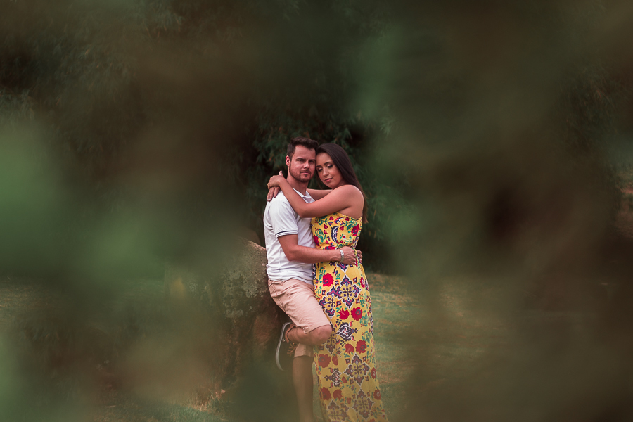 ENSAIO FOTOGRÁFICO PRÉ-WEDDING PRE WEDDING PREWEDDING DE CASAL PARQUE DO JAPAO MARINGA PARANA EM MEIO AS ARVORES APARECEM APENAS OS NOIVOS ABRACADOS ENQUANTO O NOIVO OLHA DIRETAMENTE PARA A CAMERA EM UM SINAL DE PROTECAO A NOVIA QUE DESCANSA