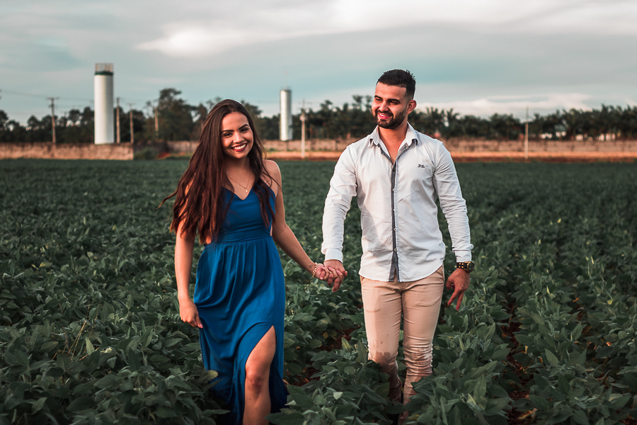 ENSAIO PRE WEDDING MANDAGUACU PARANA PRE CASAMENTO MARINGA CASAL ANDANDO NA SOJA DE MAOS DADAS FOTO DE FRENTE A MULHER ESTA SORRINDO E OLHANDO PARA A CAMERA E ELE ESTA OLHANDO PARA ELA 