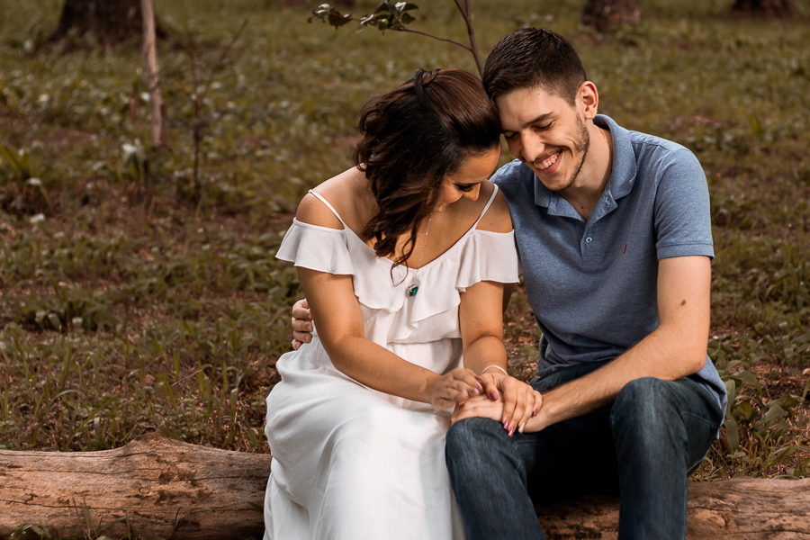 PRE CASAMENTO REALIZADO NO BOSQUE DAS GREVILEAS E NA LINHA DO TREM EM MARINGA NO PARANA CASAL ESTÁ SENTADO EM UM TRONCO SORRINDO