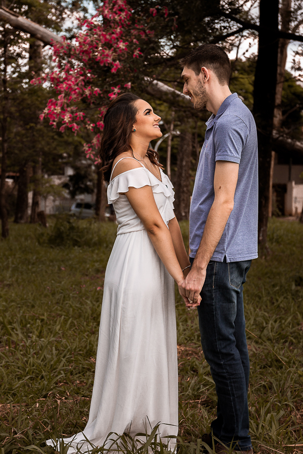 PRE CASAMENTO REALIZADO NO BOSQUE DAS GREVILEAS E NA LINHA DO TREM EM MARINGA NO PARANA NA IMAGEM O CASAL APARECE SORRINDO UM PARA O OUTRO COM UMA ARVORA FLORIDA DE FUNDO