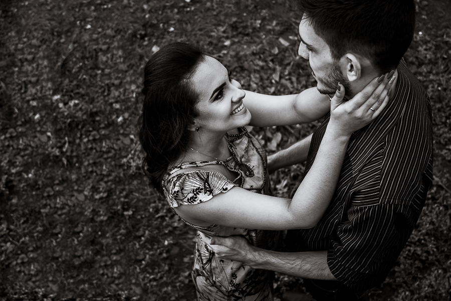 PRE CASAMENTO REALIZADO NO BOSQUE DAS GREVILEAS E NA LINHA DO TREM EM MARINGA NO PARANA NA IMAGEM DE UM ANGULO ALTO A NOIVA FAZ CARINHO COM AS DUAS MAOS NO PESCOÇO DO NOIVO ENQUANTO SORRI PARA ELE