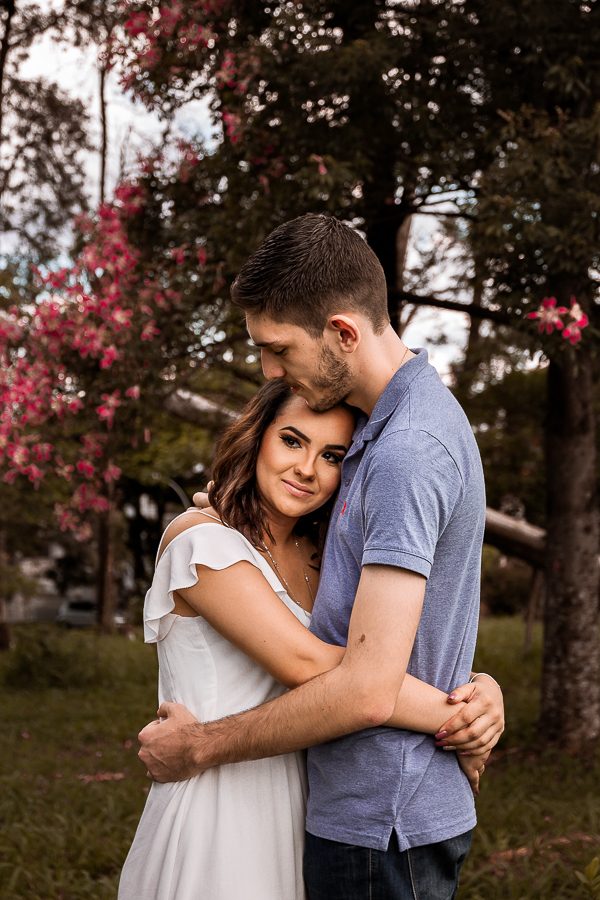 PRE CASAMENTO REALIZADO NO BOSQUE DAS GREVILEAS E NA LINHA DO TREM EM MARINGA NO PARANA NA IMAGEM A NOIVA APARECE DEITADA NO PEITO DO NOIVO QUE ACARICIA SEU BRACO COM FUNDO PARA UMA ARVORE FLORIDA