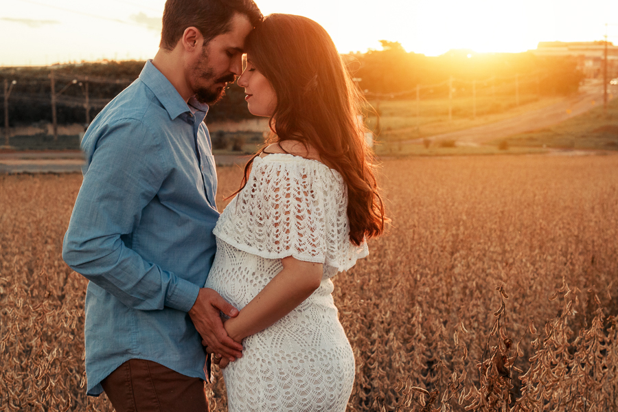 ENSAIO FOTOGRAFICO DE GESTANTE GESTACAO REALIZADO EM MARINGA NO PARANA NA IMAGEM A MAMAE APARECE COM UM VESTIDO BRANCO NA FOTO O CASAL SEGURA A BARRIGA COM O ANTONIO PARA FAZER CARINHO E SENTIR A ANSIEDADE DO PRIMEIRO FILHO UMA LUZ AMARELADA INVADE FUNDO