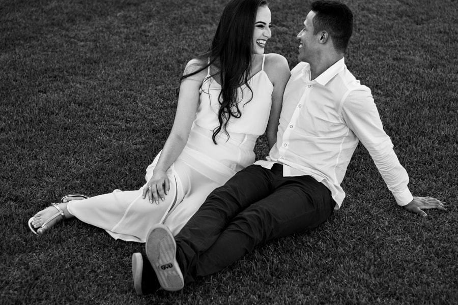 CASAMENTO OU PRE WEDDING REALIZADO EM MARINGA PARANA COM UM CASAL JOVEM A CEU ABERTO NA IMAGEM O CASAL ESTA SENTADO NA GRAMA ENQUANTO SORRIEM UM PARA O OUTRO FOTO EM PRETO E BRANCO