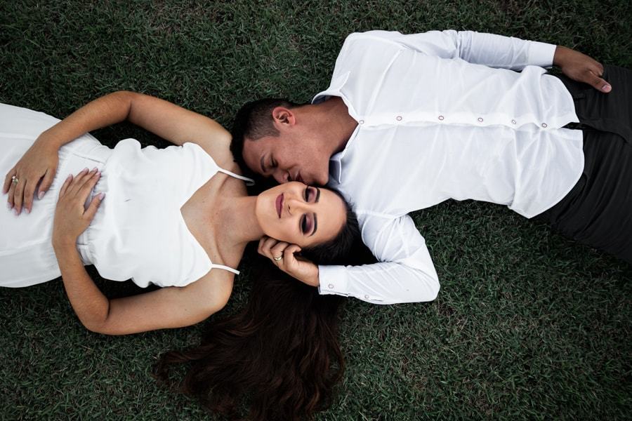 CASAMENTO OU PRE WEDDING REALIZADO EM MARINGA PARANA COM UM CASAL JOVEM A CEU ABERTO NA IMAGEM O CASAL  ESTA DEITADO NA GRAMA E O NOIVO ESTA BEIJANDO A NOIVA
