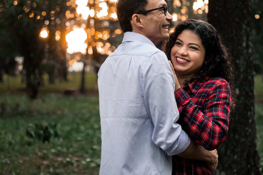 ENSAIO FOTOGRAFICO PRE CASAMENTO OU PRE WEDDING AO AR LIVRE EM BOSQUE DAS GREVILEAS GREVILIAS MARINGA NO PARANA NA IMAGEM O CASAL APARECE SORRINDO DE FRENTE UM PARA O OUTRO EM MEIO A VEGETACAO VERDE