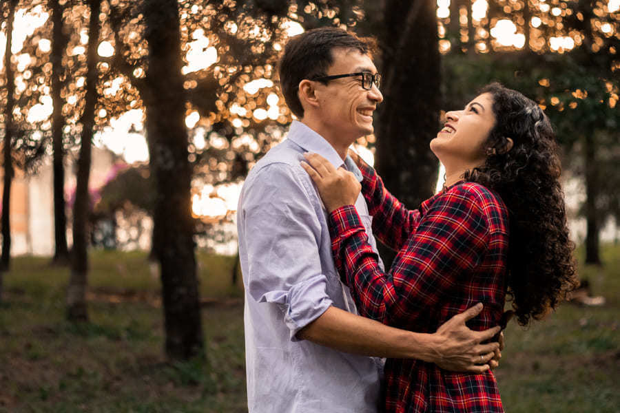 ENSAIO FOTOGRAFICO PRE CASAMENTO OU PRE WEDDING AO AR LIVRE EM BOSQUE DAS GREVILEAS GREVILIAS MARINGA NO PARANA NA IMAGEM O CASAL APARECE SORRINDO DE FRENTE UM PARA O OUTRO EM MEIO A VEGETACAO VERDE