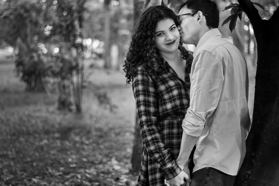 ENSAIO FOTOGRAFICO PRE CASAMENTO OU PRE WEDDING AO AR LIVRE EM BOSQUE DAS GREVILEAS GREVILIAS MARINGA NO PARANA NA IMAGEM O NOIVO ESTA ENCOSTADO EM UMA ÁRVORE ENQUANTO A NOIVA OLHA PARA A CAMERA FOTO EM PRETO E BRANCO