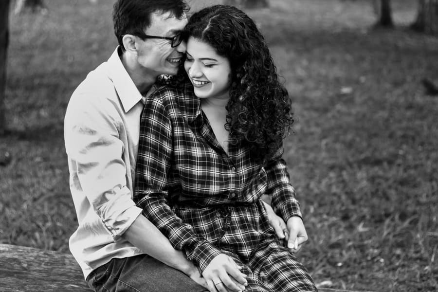 ENSAIO FOTOGRAFICO PRE CASAMENTO OU PRE WEDDING AO AR LIVRE EM BOSQUE DAS GREVILEAS GREVILIAS MARINGA NO PARANA NA IMAGEM O CASAL ESTA SENTADO EM UM BANCO TROCANDO CARINHOS E SORRISOS FOTO EM PRETO E BRANCO