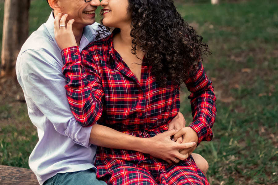 ENSAIO FOTOGRAFICO PRE CASAMENTO OU PRE WEDDING AO AR LIVRE EM BOSQUE DAS GREVILEAS GREVILIAS MARINGA NO PARANA NA IMAGEM O CASAL ESTA SENTADO EM UM BANCO TROCANDO CARINHOS E SORRISOS