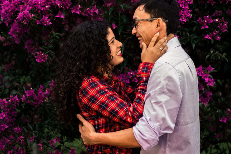 ENSAIO FOTOGRAFICO PRE CASAMENTO OU PRE WEDDING AO AR LIVRE EM BOSQUE DAS GREVILEAS GREVILIAS MARINGA NO PARANA NA IMAGEM O CASAL APARECE EM FRENTE A MUITAS FLORES ROSADAS TROCANDO CARINHOS E AFETOS E SORRINDO MUITO