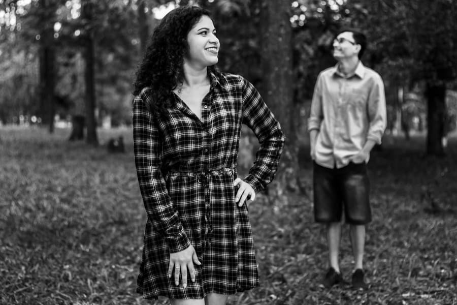 ENSAIO FOTOGRAFICO PRE CASAMENTO OU PRE WEDDING AO AR LIVRE EM BOSQUE DAS GREVILEAS GREVILIAS MARINGA NO PARANA NA IMAGEM O CASAL APARECE SEPARADOS EM DOIS PLANOS A NOIVA NA FRENTE E O NOIVO NO FUNDO OS DOIS SORRIEM OLHANDO NA DIRECAO UM DO OUTRO