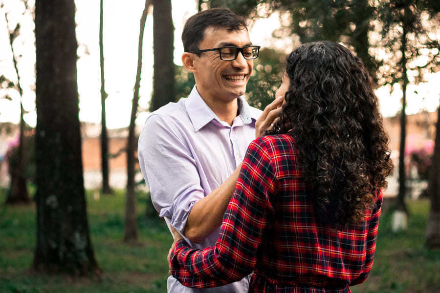 ENSAIO FOTOGRAFICO PRE CASAMENTO OU PRE WEDDING AO AR LIVRE EM BOSQUE DAS GREVILEAS GREVILIAS MARINGA NO PARANA NA IMAGEM O CASAL APARECE SORRINDO DE FRENTE UM PARA O OUTRO EM MEIO A VEGETACAO VERDE