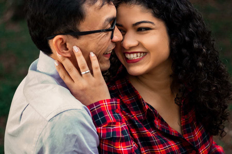 ENSAIO FOTOGRAFICO PRE CASAMENTO OU PRE WEDDING AO AR LIVRE EM BOSQUE DAS GREVILEAS GREVILIAS MARINGA NO PARANA NA IMAGEM O CASAL ESTA SENTADO EM UM BANCO TROCANDO CARINHOS E SORRISOS
