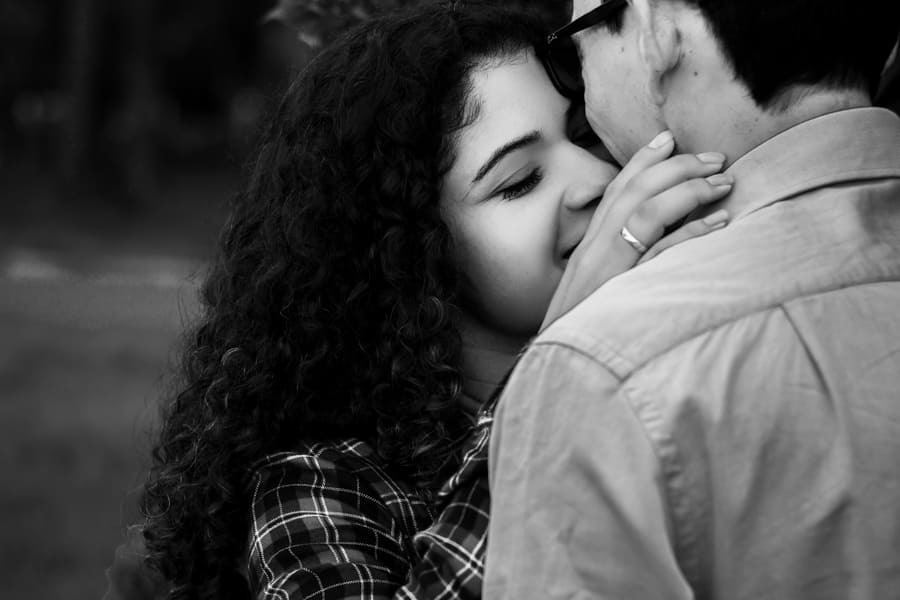ENSAIO FOTOGRAFICO PRE CASAMENTO OU PRE WEDDING AO AR LIVRE EM BOSQUE DAS GREVILEAS GREVILIAS MARINGA NO PARANA NA IMAGEM O CASAL APARECE EM FRENTE A MUITAS FLORES ROSADAS TROCANDO CARINHOS E AFETOS E SORRINDO MUITO FOTO EM PRETO E BRANCO