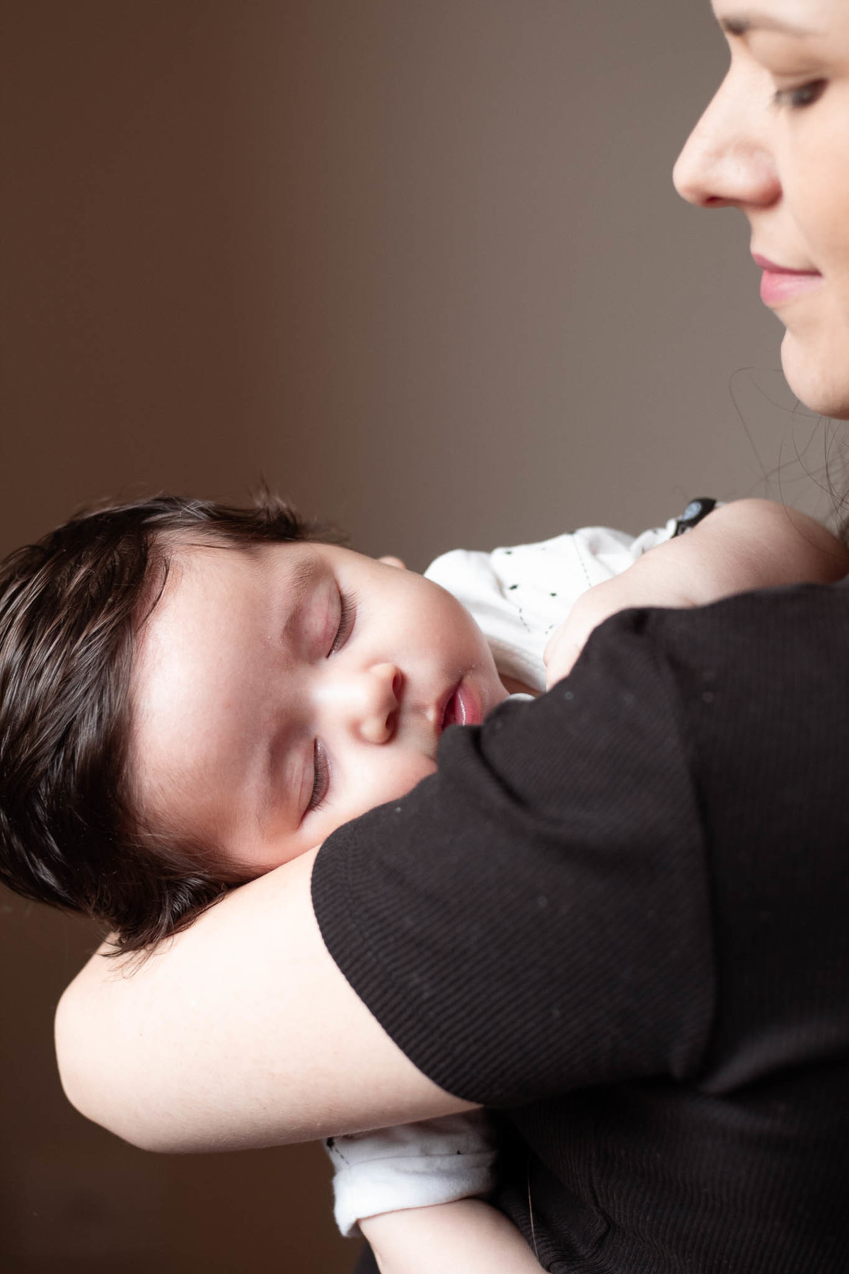 bebê de pele clara, cabelos e olhos castanho escuro, dormindo nos braços da mãe.