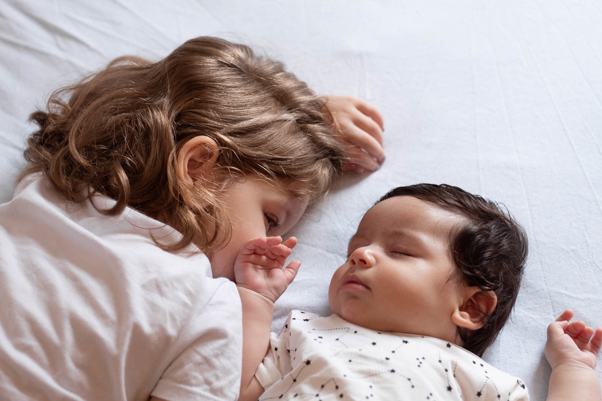 bebê de pele clara, cabelos e olhos castanho escuro, dormindo com sua irmã, uma menina loira de 5 anos
