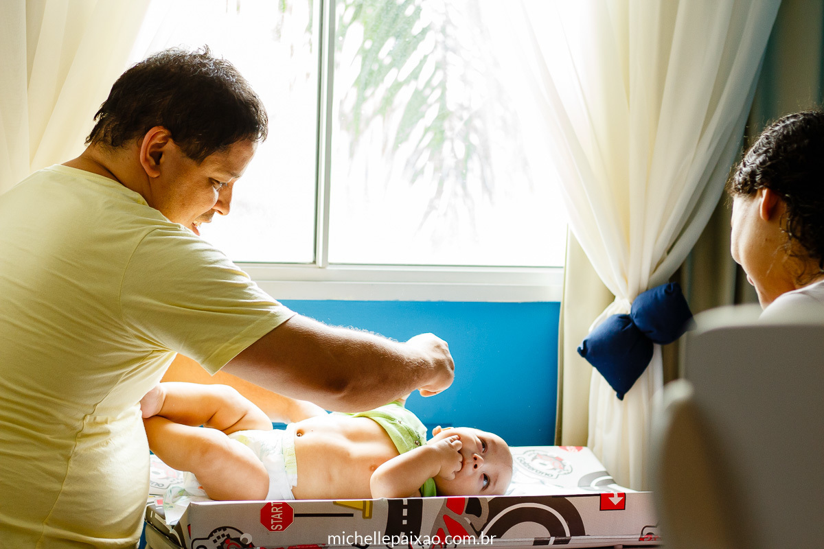 ensaio bebê estilo lifestyle fotografia da rotina do bebê pai trocando bebê no trocador com suporte de pista de corrida carros rio de janeiro