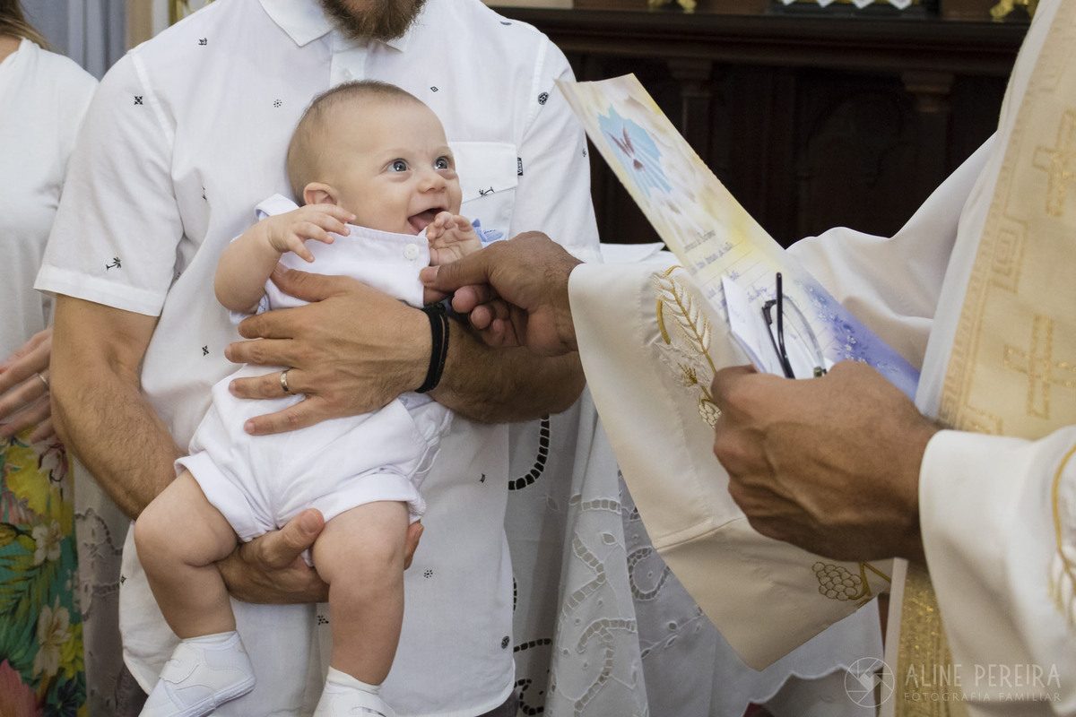 Padre fazendo graça com o bebê durante o batizado