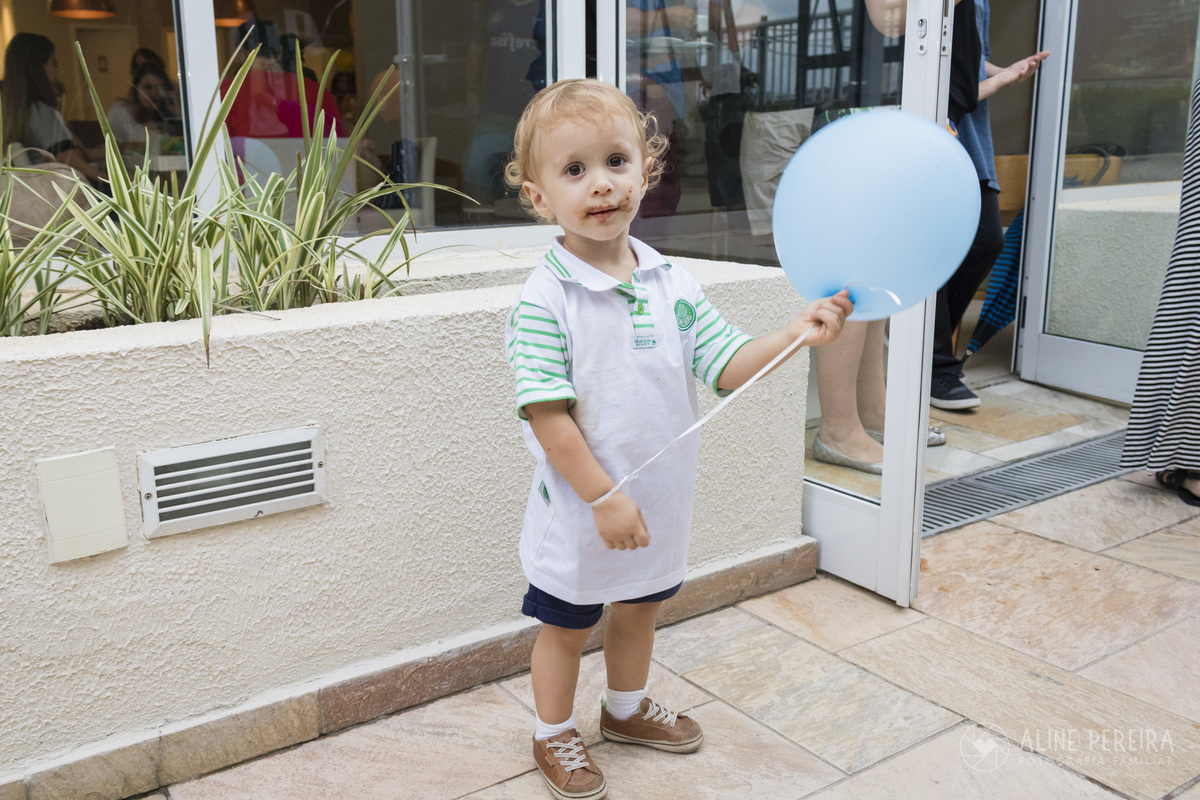 criança segurando um balão com a boca toda suja de chocolate