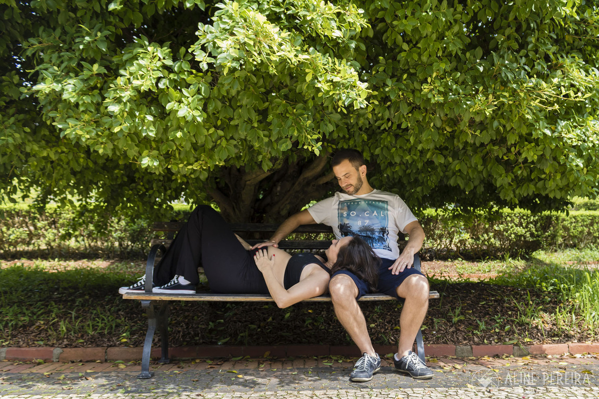 grávida deitada no colo do marido num banco de praça