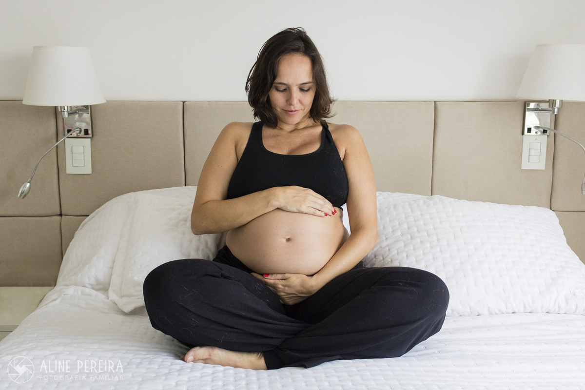 grávida posando com as mãos na barriga sentada na cama de sua casa
