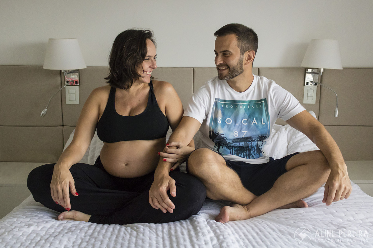 casal a espera do primeiro filho sentados na cama de sua casa