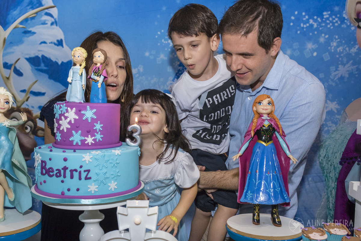 aniversariante apagando a vela do bolo na mesa decorada com o tema frozen