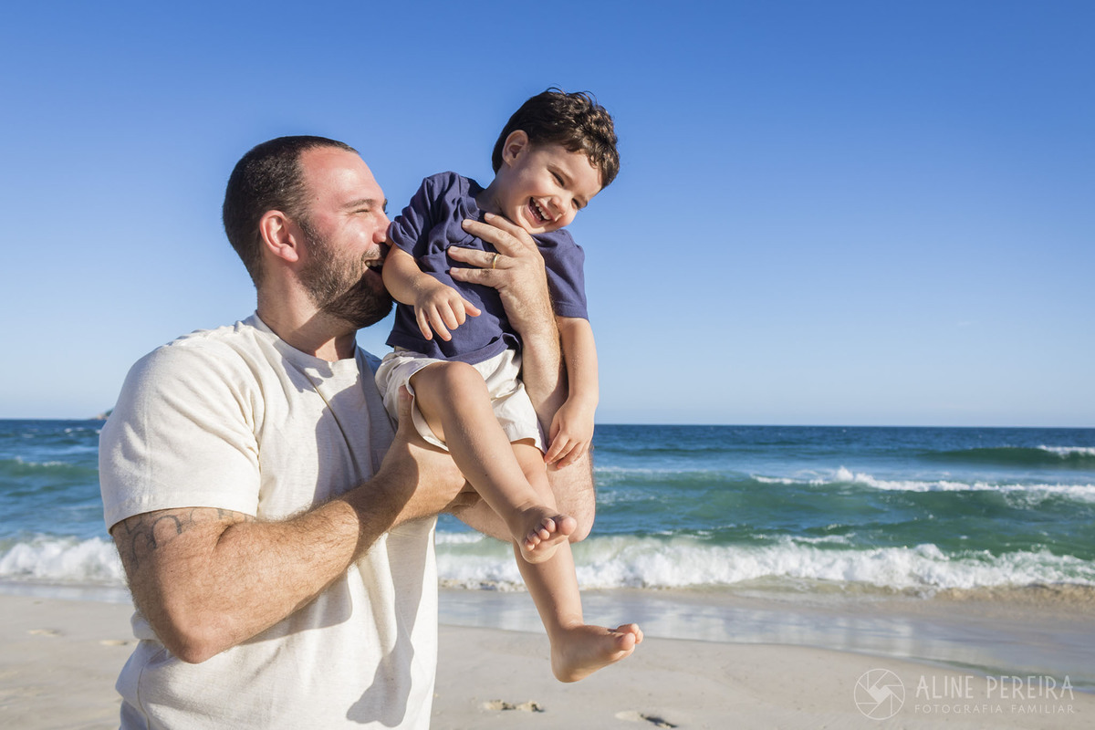 Pai brincando com o filho no colo na praia da Barra da Tijuca