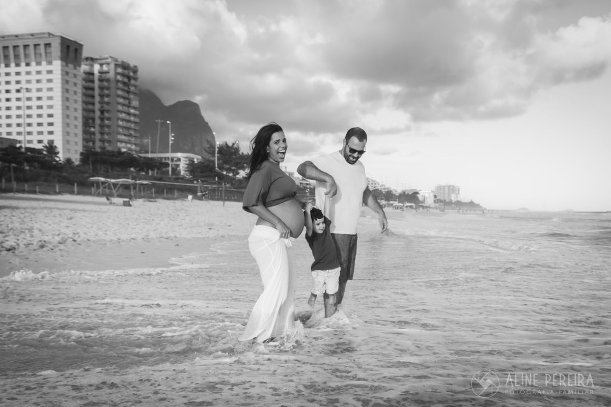 pai e mãe grávida balançando o filho pequeno em cima do mar na praia da Barra da Tijuca