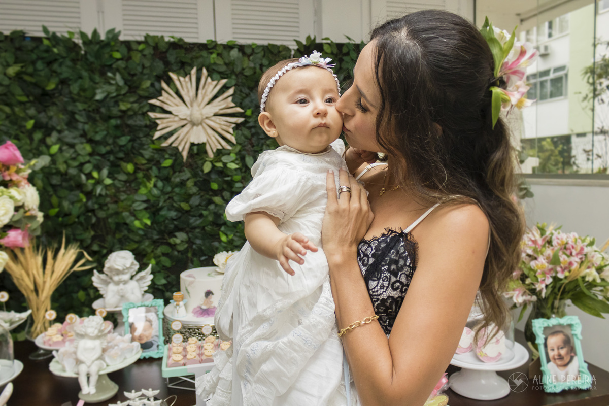 mae beijando a filha em frente a mesa decorada do batizado
