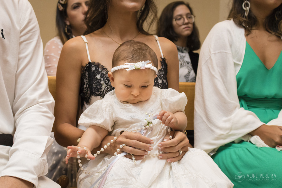 menina segurando um terço em seu batizado
