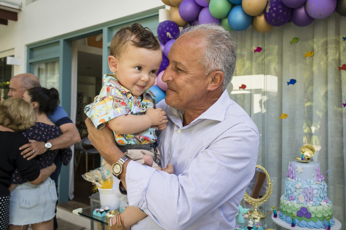 menino no colo do avô em frente a mesa do bolo