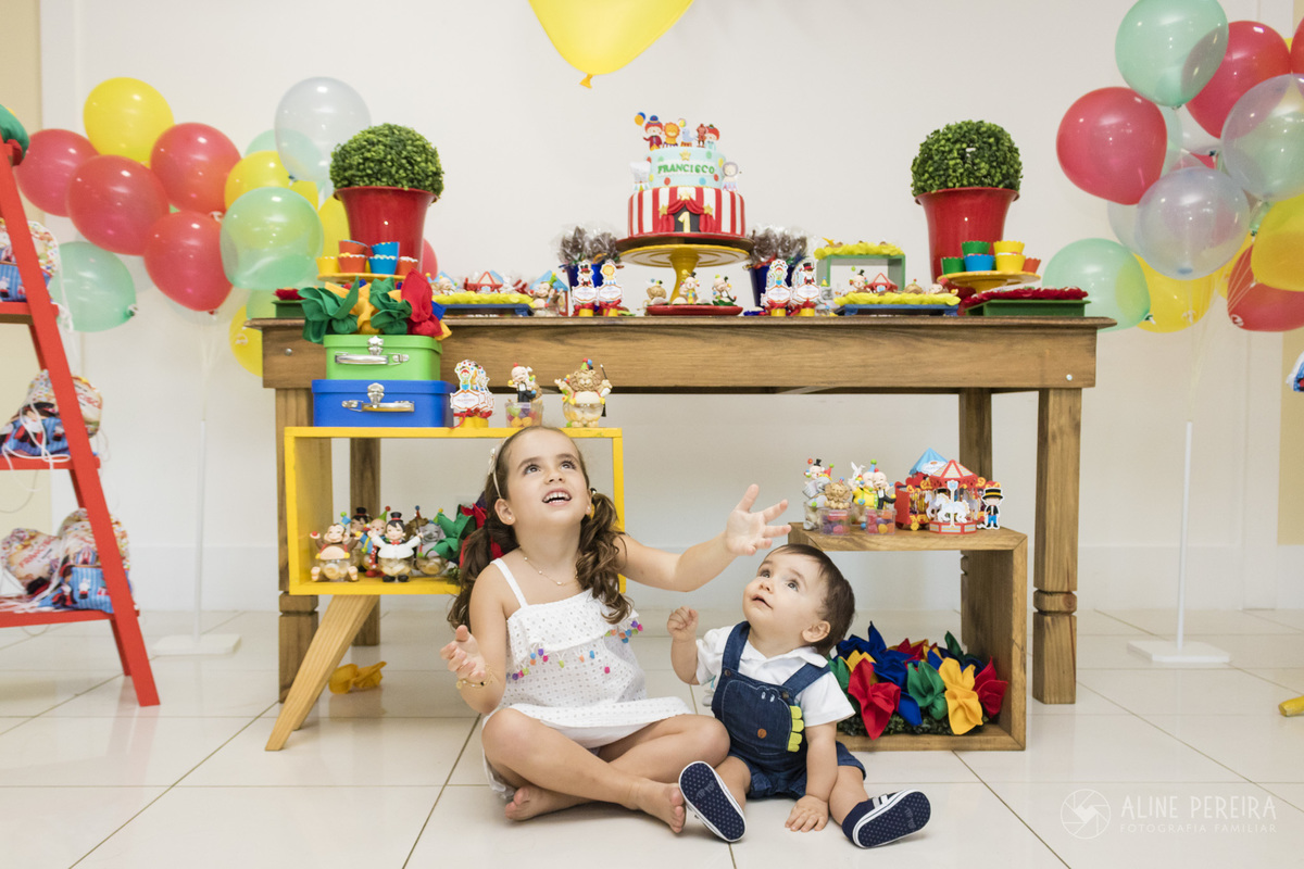 menino e menina sentados em frente a mesa do bolo decorada com o tema circo brincando com uma bola