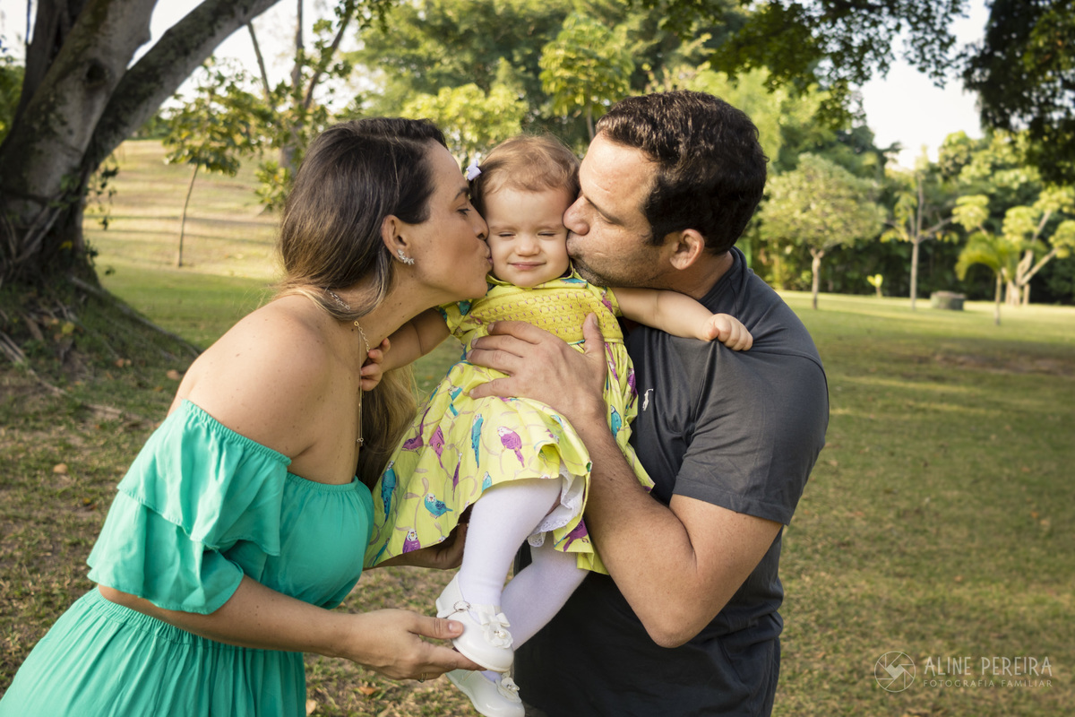 pai e mãe dando um beijo sanduiche na criança no parque