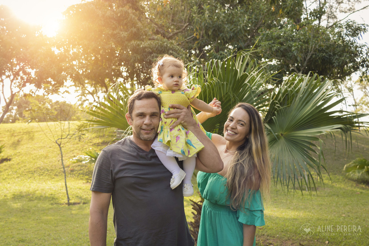 familia de pai, mãe e menina no parque com sol ao fundo