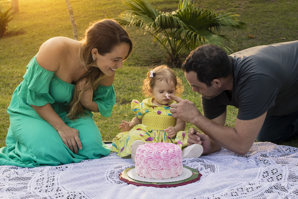 pai sujando o nariz da filha com o bolo de aniversário