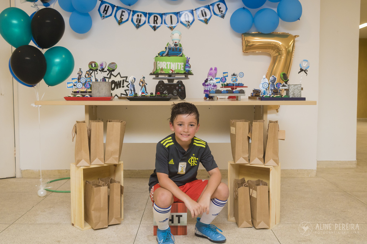 menino em frente a mesa do bolo com o tema fortnite