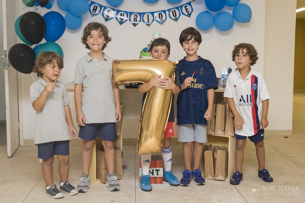 crianças em frente a mesa do bolo com o tema fortnite segurando um balão com o numero 7