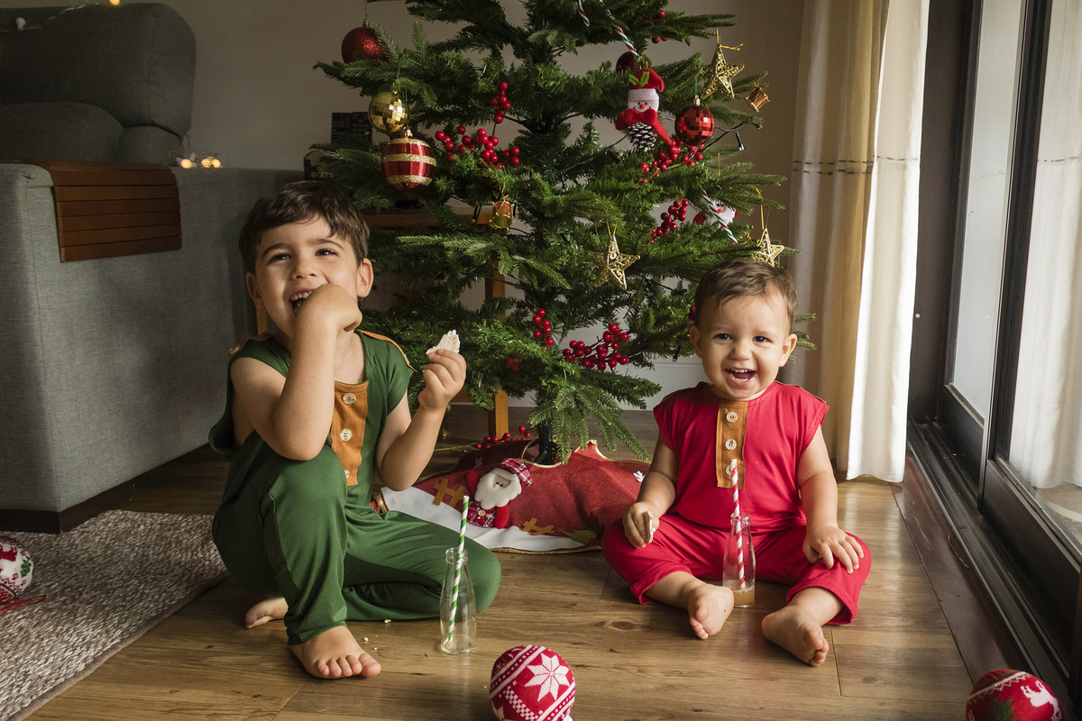 crianças brincando e sorrindo em frente a árvore de natal em casa