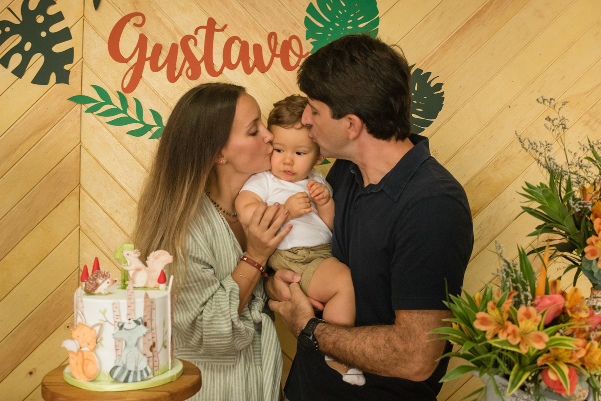 pais beijando o filho na mesa do bolo decorada com o tema floresta
