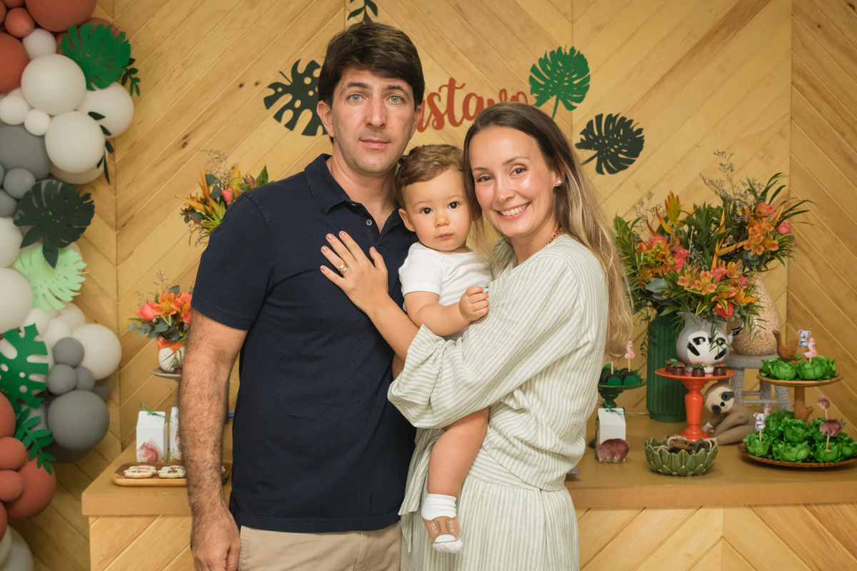 pai, mãe e criança em frente a mesa decorada com o tema floresta