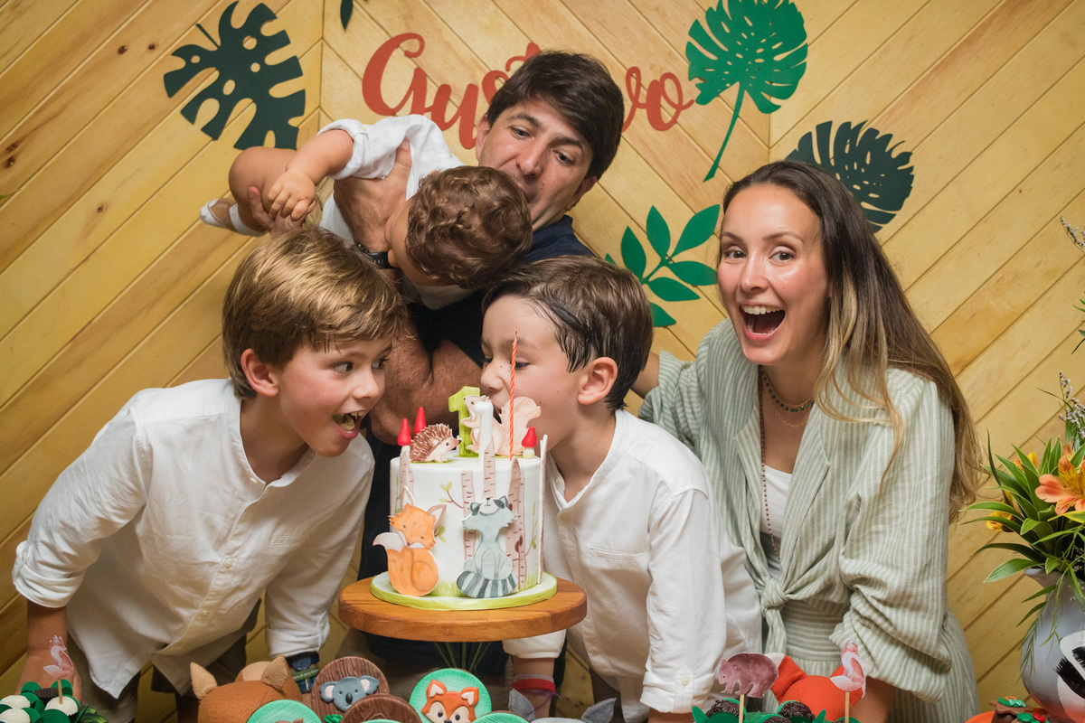 crianças fingindo que vão morder o bolo na mesa de aniversário com o tema floresta