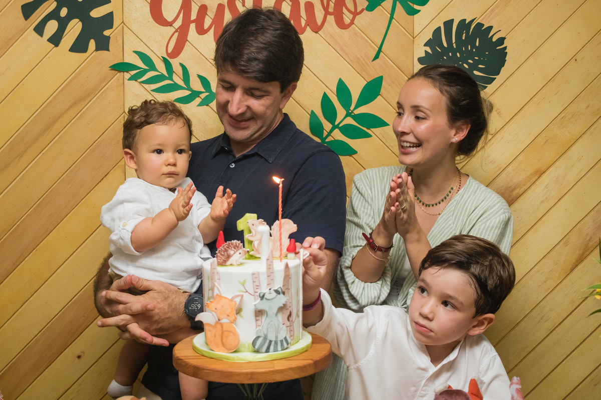 criança de 1 ano batendo palminhas na mesa do bolo de seu aniversário com o tema floresta