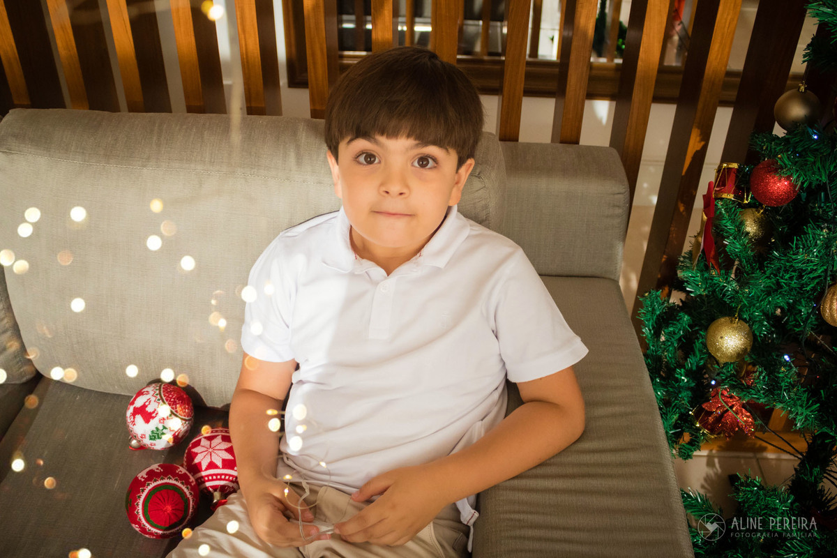 menino sentado no sofa com luzes e bolas de natal